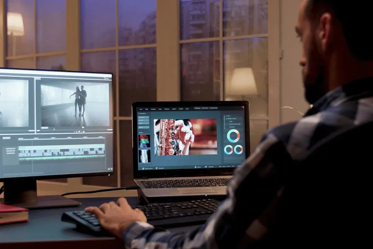 A man edits video on dual-screen setup at night, focusing on visuals of dancers and a saxophone, with modern editing software displayed.