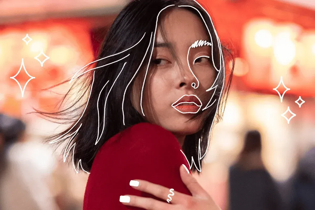 Une femme aux cheveux foncés porte un haut rouge et affiche une expression songeuse. Des traits blancs soulignent ses traits sur un arrière-plan flou aux tons chauds.