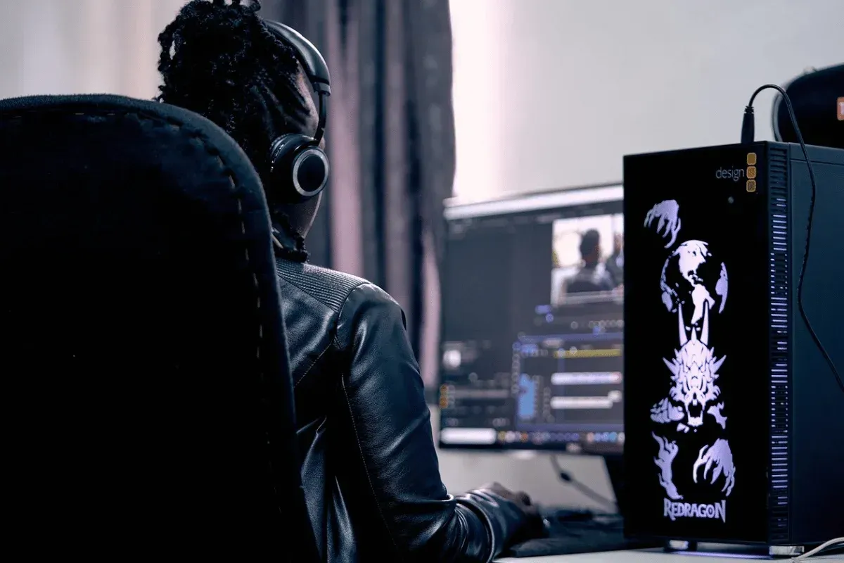 Une personne portant un casque et une veste en cuir effectue un montage sur deux écrans affichant un logiciel de montage vidéo.