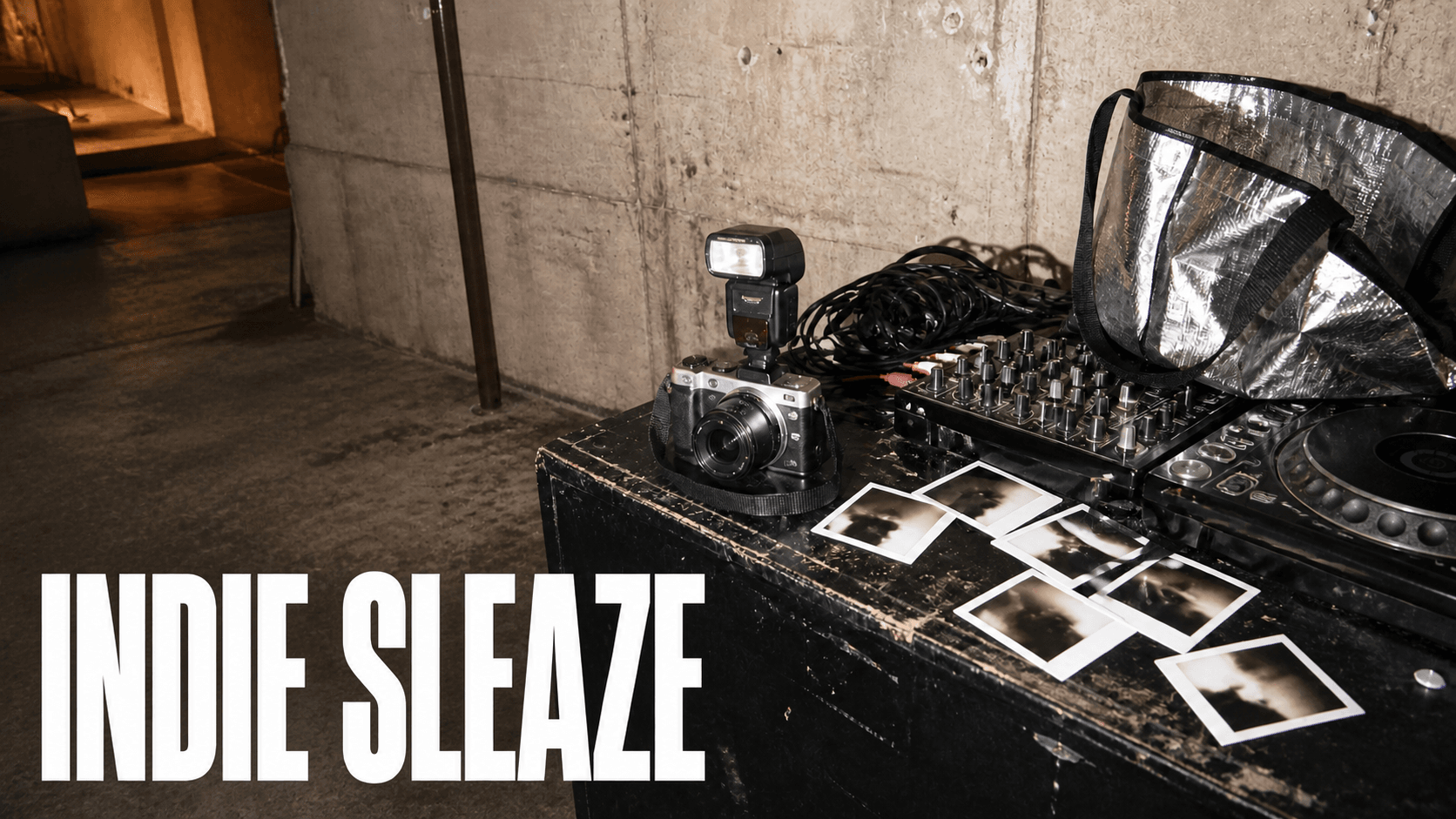 A compact camera with an external flash and instant photo prints on a scuffed road case beside a DJ mixer in a concrete basement. Overlaid title: Indie Sleaze.